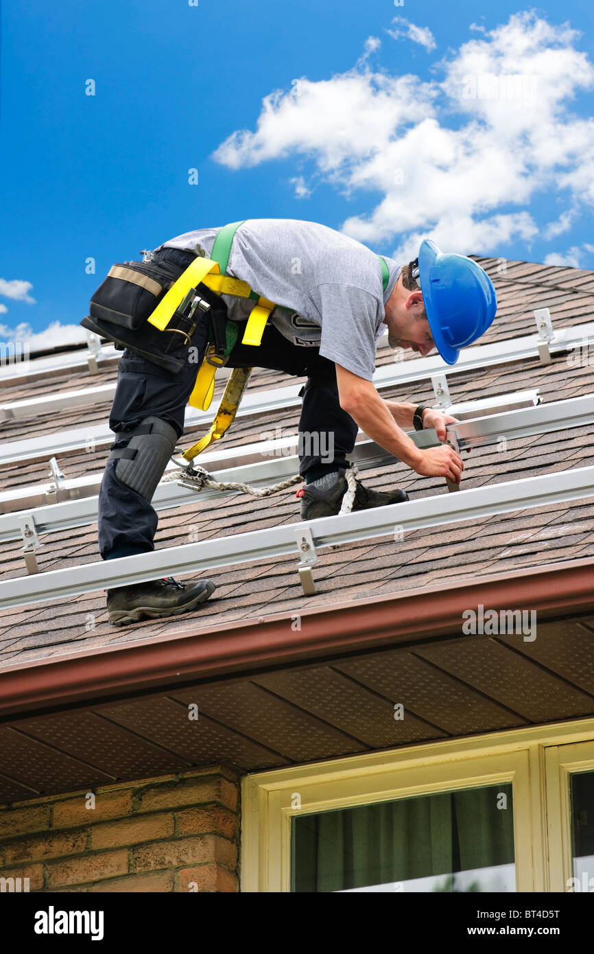 Uomo di installare guide per pannelli solari sulla casa residenziale tetto Foto Stock