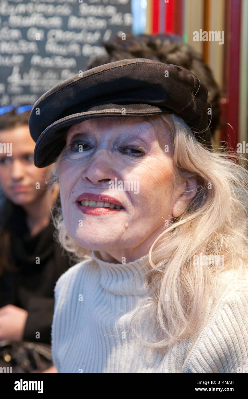Signora di una certa età seduta a Parigi cafe abilmente fatta con chic casquette in cima i suoi lunghi capelli biondi Foto Stock
