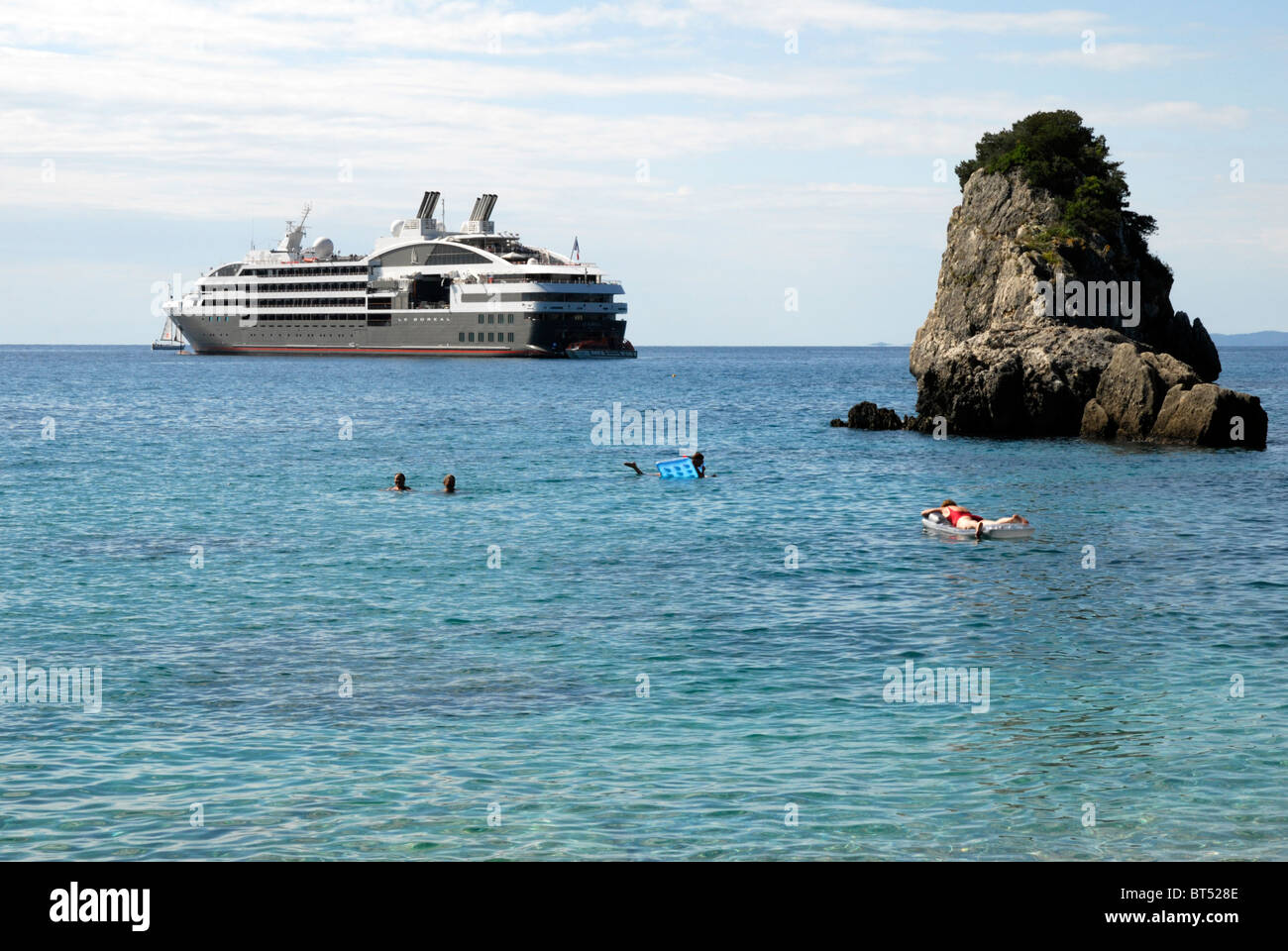 Lussuosa nave da crociera che sono ancorate al largo di Piso Kryoneri spiaggia di Parga, Epiro, Grecia. I nuotatori in primo piano. Foto Stock