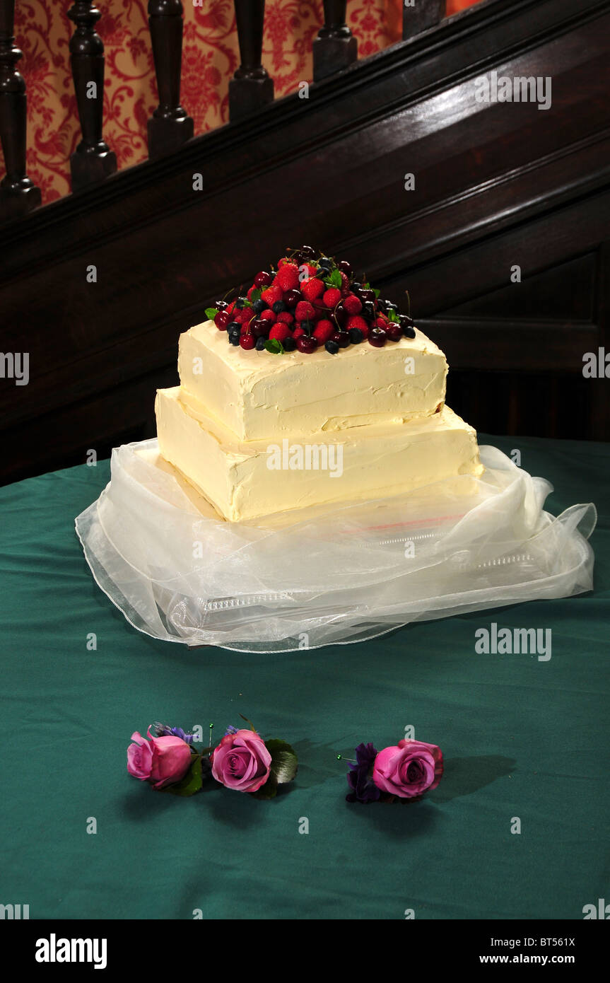 Un color crema due tiered torta di nozze con fresca frutta estiva sulla parte superiore e tre rose, foro di pulsante di fiori. Maggio 2010 Foto Stock