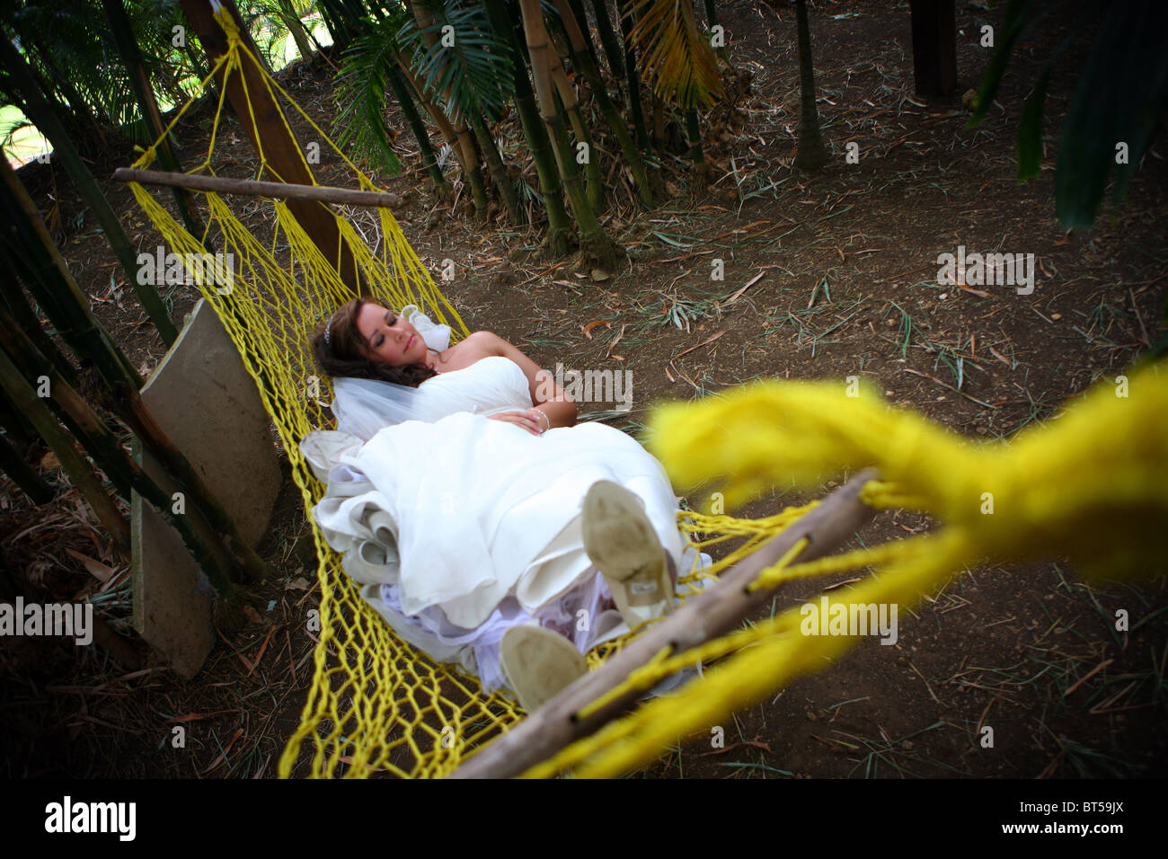 Sposa per rilassarsi in un'amaca in giardini tropicali a un matrimonio d'oltremare Foto Stock