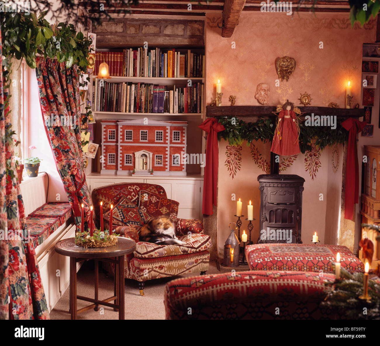 Le candele accese il camino con stufa a legna in cottage soggiorno decorato per il Natale con le bambole rosso-house sugli scaffali Foto Stock