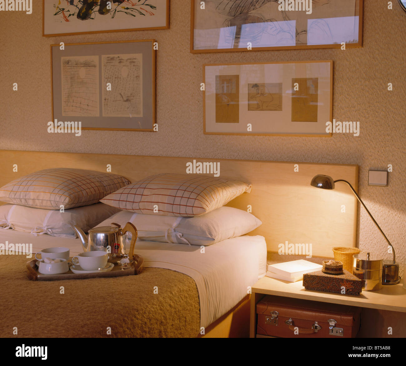 Illuminati moderna lampada sul comodino accanto al letto con cuscini impilati e vassoio di prima colazione Foto Stock