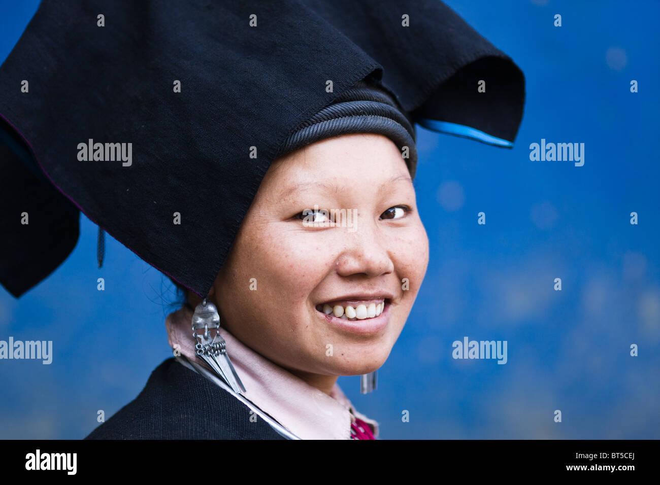 Un Nero Dzao donna che indossa abiti tradizionali sorridere per la fotocamera mentre si sta in piedi di fronte ad una parete blu Foto Stock