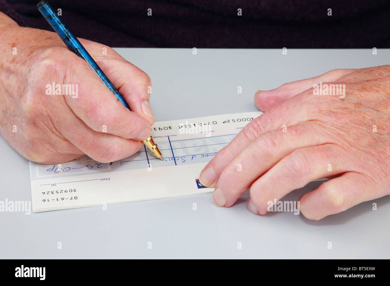 Close-up di un senior donna anziana pensionata scrivendo un check (controllo) per pagare una bolletta. Inghilterra, Regno Unito, Gran Bretagna. Foto Stock