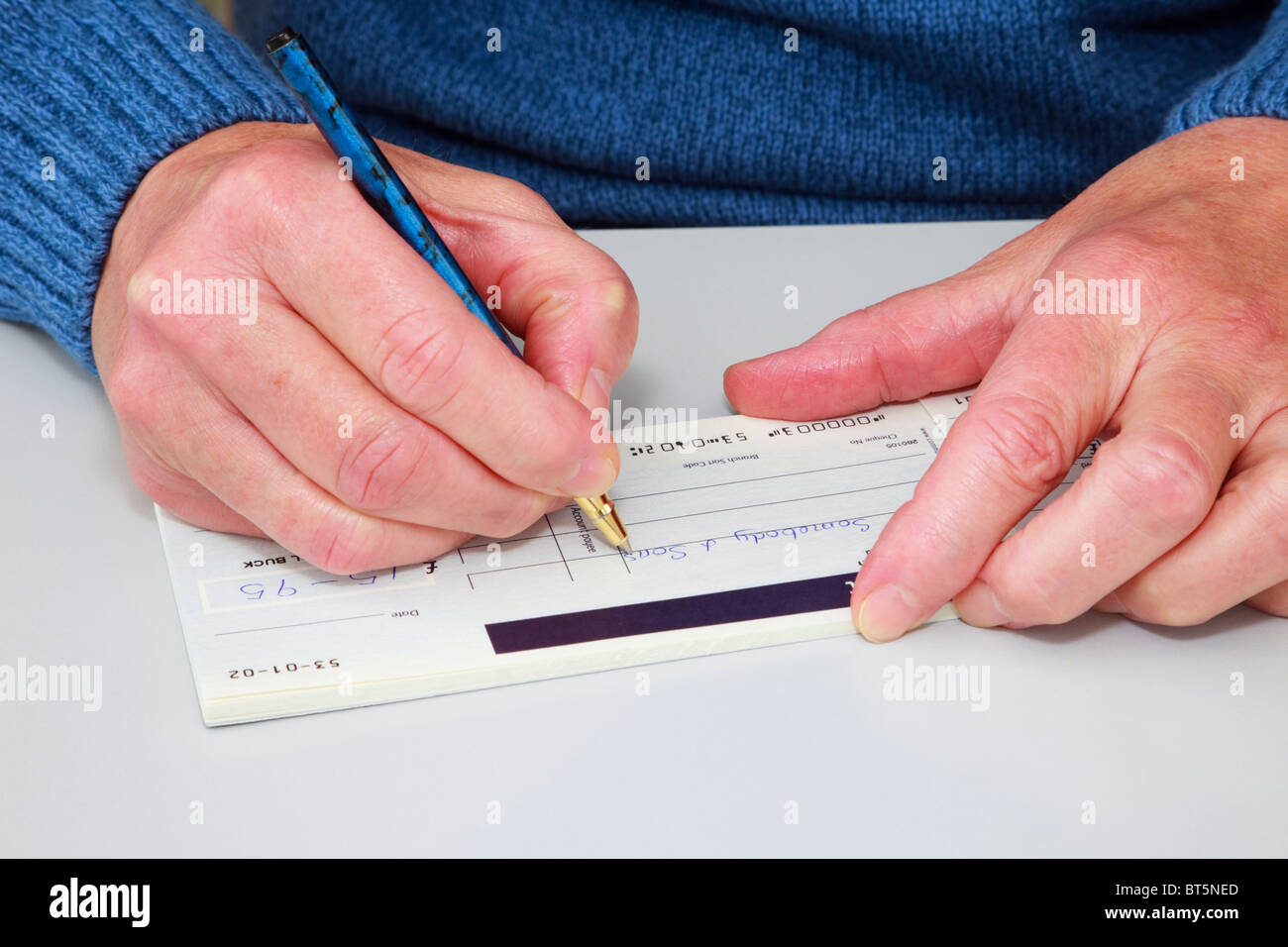 Close-up di una donna matura la scrittura di un controllo (controllo) in un libretto di assegni per pagare una bolletta. Inghilterra, Regno Unito, Gran Bretagna. Foto Stock