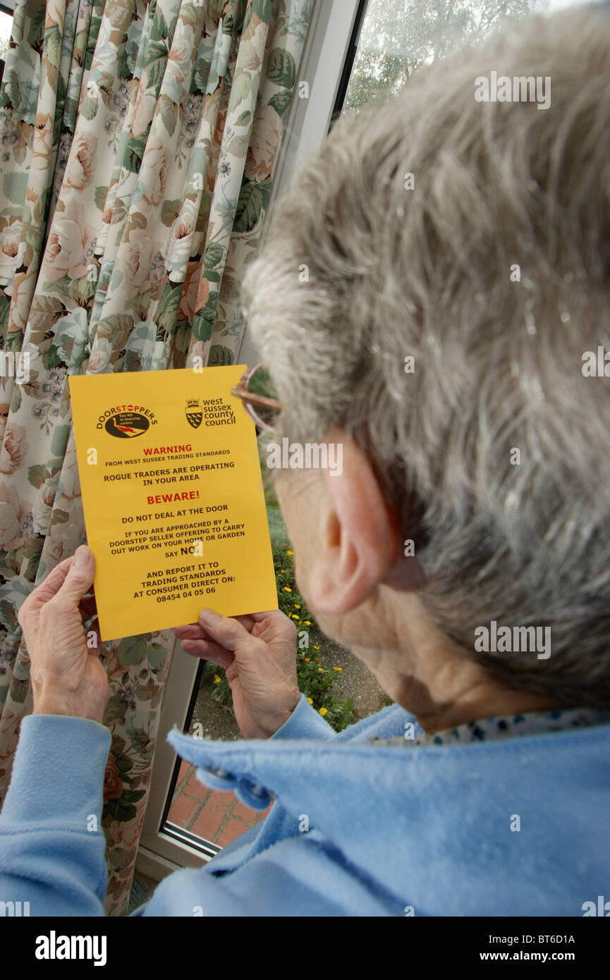 Donna anziana la lettura di un messaggio di avviso opuscolo informativo circa i commercianti disonesti & venditori a domicilio Foto Stock