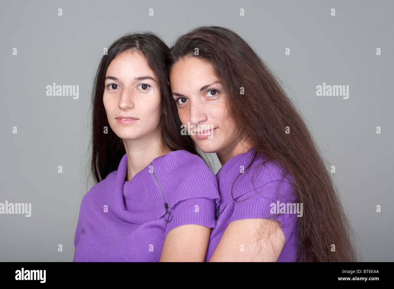 Ritratto di due sorelle con lunghissimi capelli castani -isolato su grigio Foto Stock