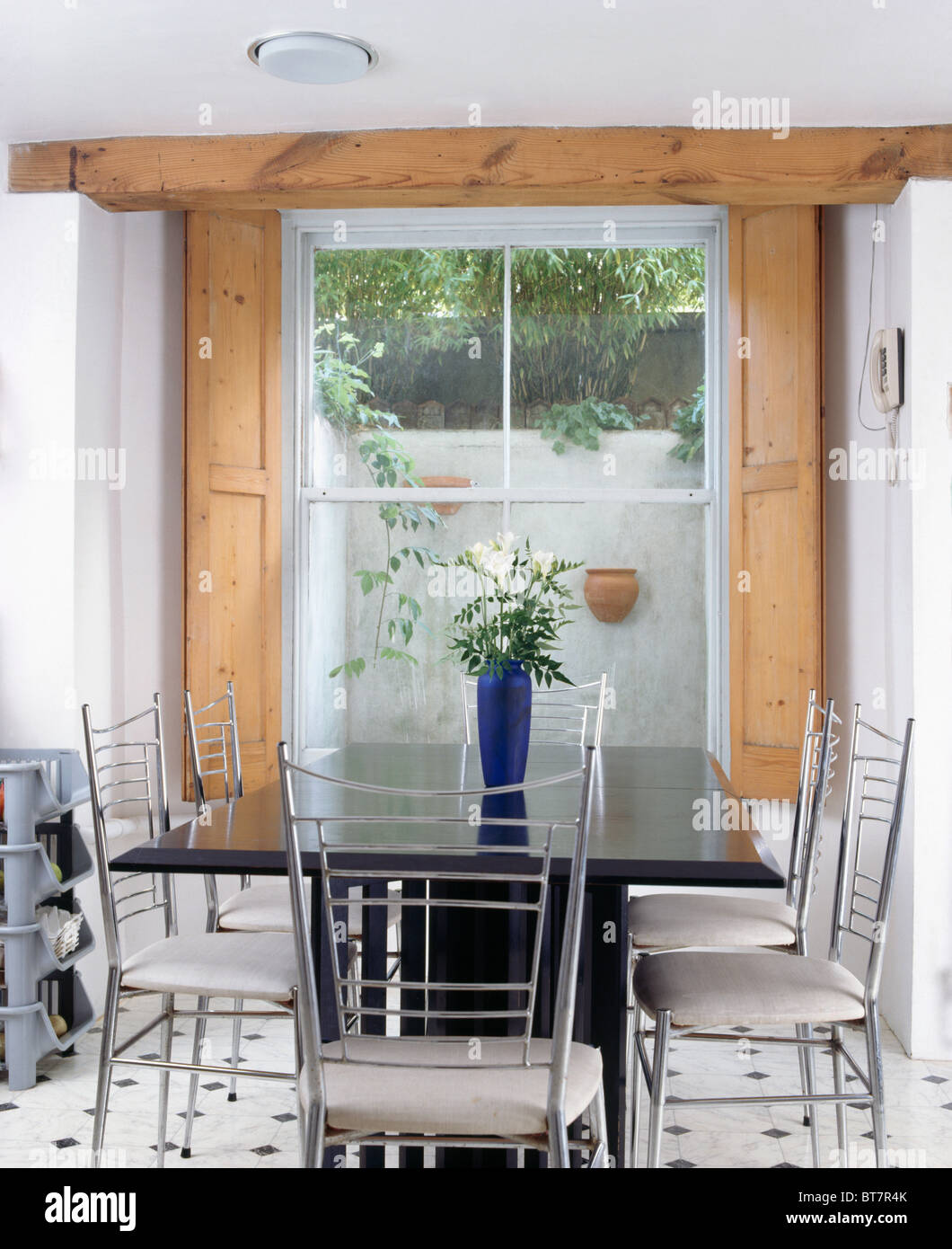 Metallo e sedie bianche a tavola nera nel seminterrato moderna sala da pranzo con persiane di legno in corrispondenza della finestra Foto Stock