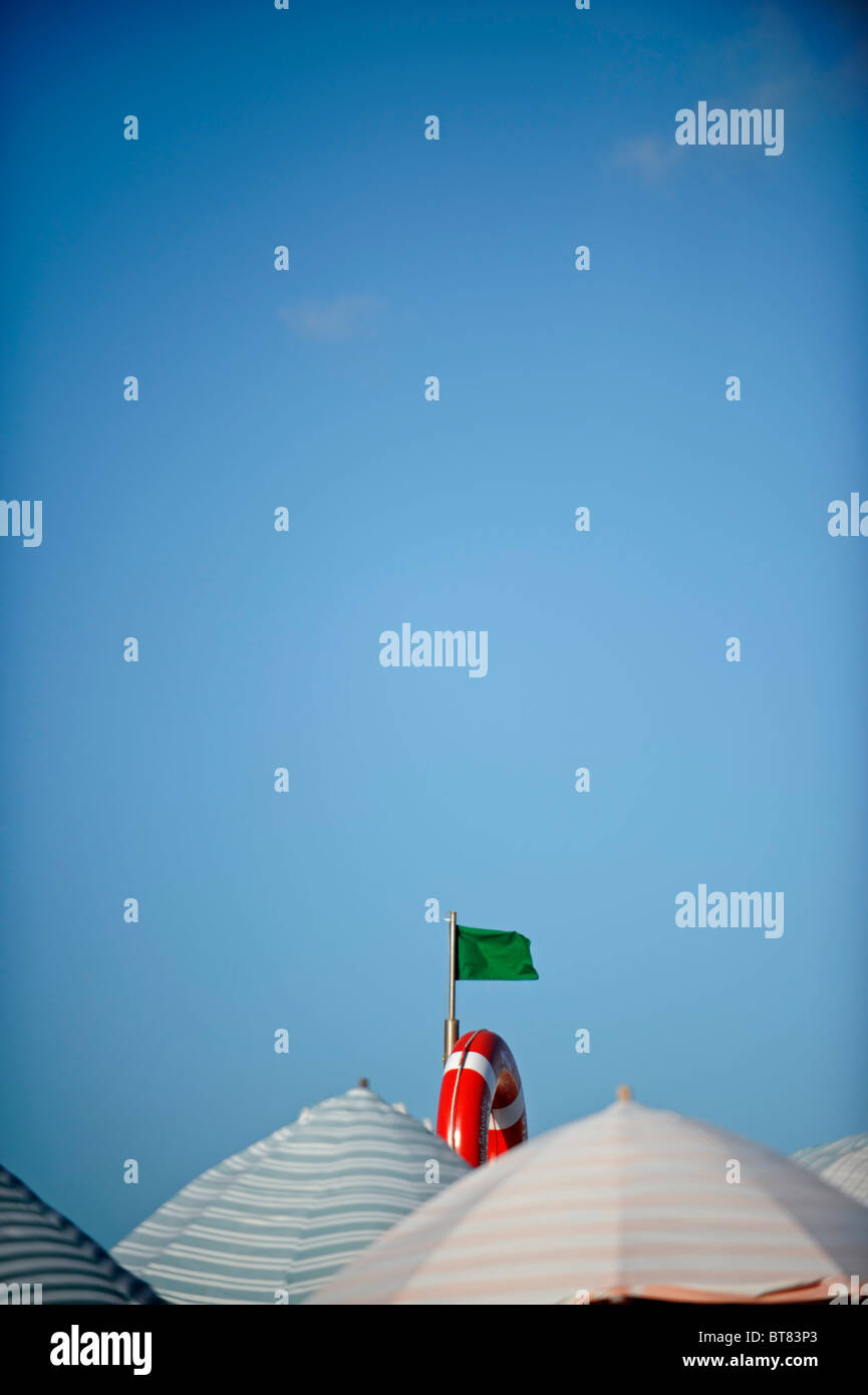 Bandiera verde, anello ancora di salvezza e striato ombrelloni contro un cielo blu Foto Stock