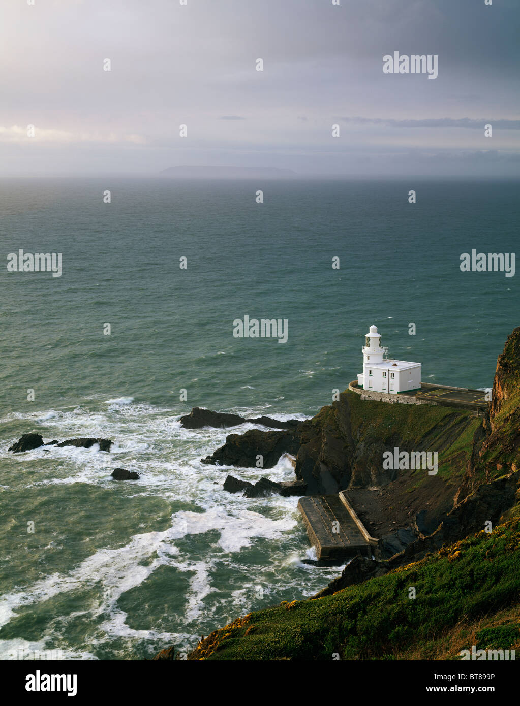 Faro di Hartland Point sulla costa nord del Devon vicino a Hartland, Inghilterra. Lundy Island è visibile all'orizzonte nella nebbia. Foto Stock