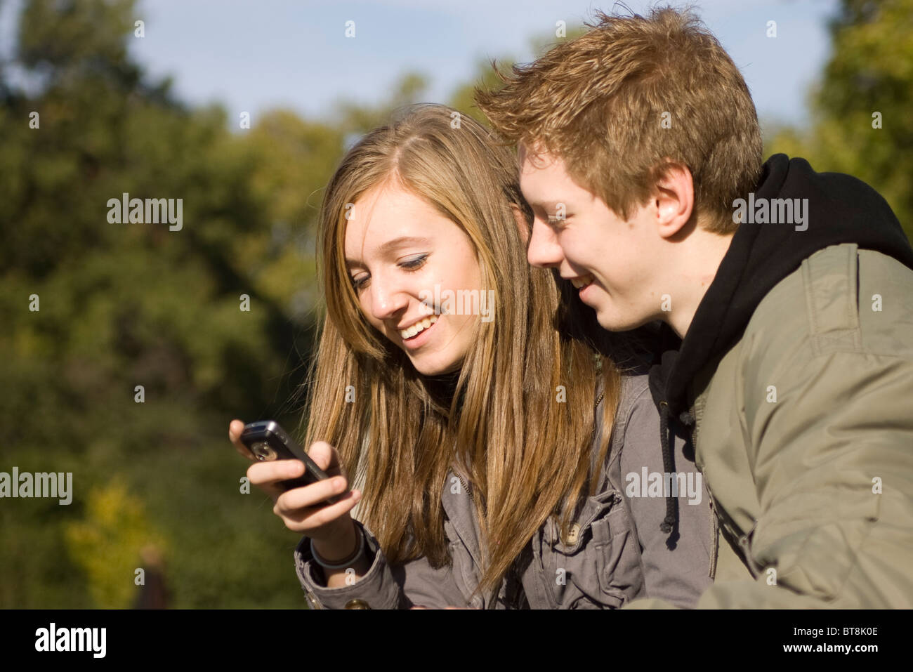 Ragazzo adolescente e una ragazza nel parco guardando il telefono cellulare insieme, condividendo, sorridente Foto Stock