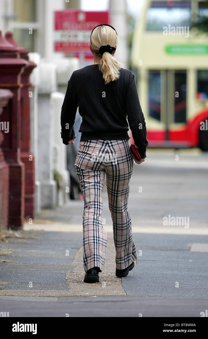 Una donna che indossa Burberry controllare i pantaloni passeggiate lungo la strada. Foto di James Boardman. Foto Stock
