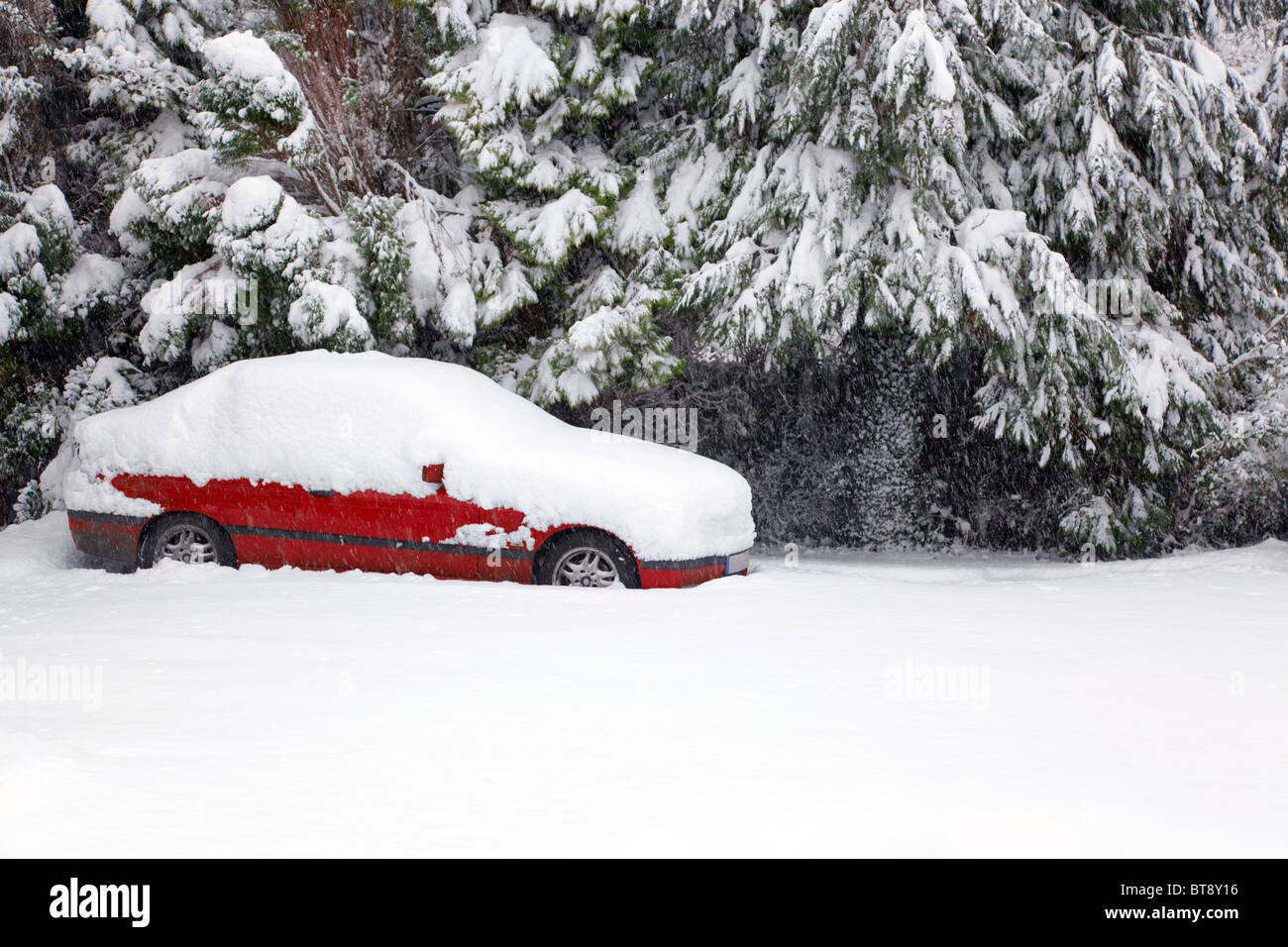 Un auto rossa coperto di neve fresca abbandonati nella strada durante una bufera di neve. Foto Stock