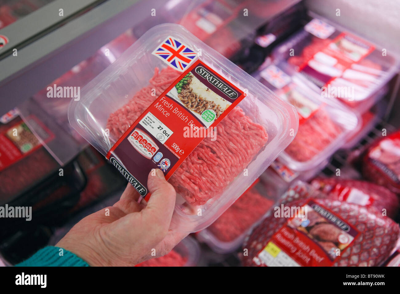 Una donna femmina shopper scegliendo un pacchetto di British carni bovine macinate imballaggi in plastica con le etichette dei prodotti alimentari ad acquistare da un supermercato frigorifero. Regno Unito Foto Stock