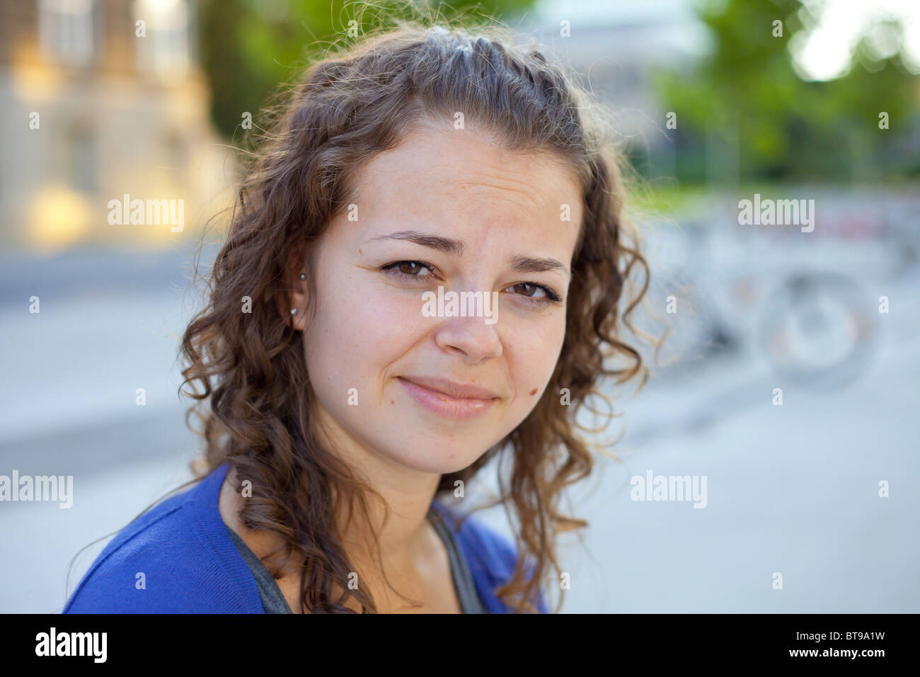 Giovane donna con capelli marroni ricci che strisciano guardando di lato, all'aperto con luce naturale Foto Stock