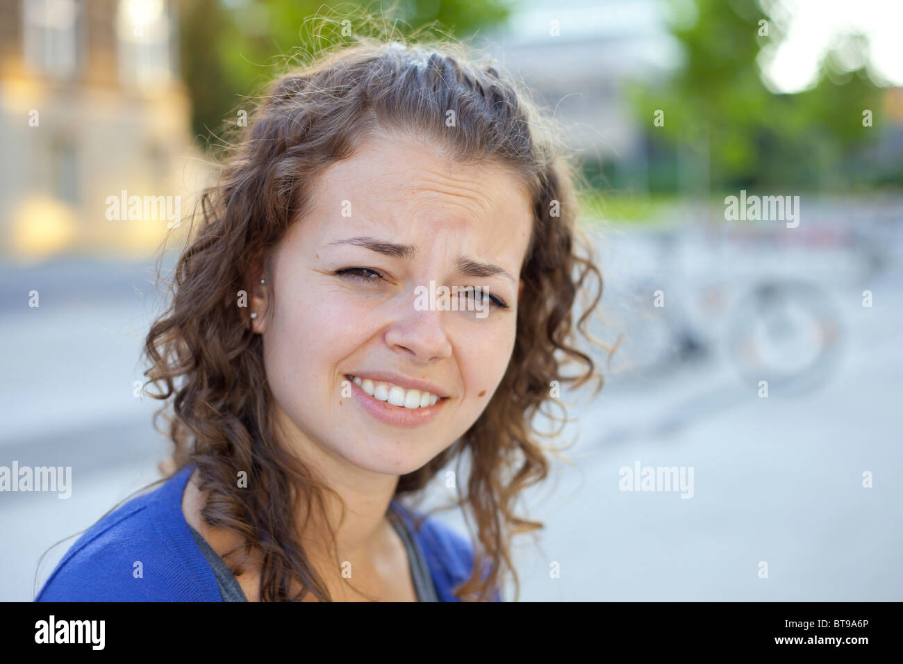 Una giovane donna che dona una scomoda espressione all'aperto, alla luce del giorno Foto Stock