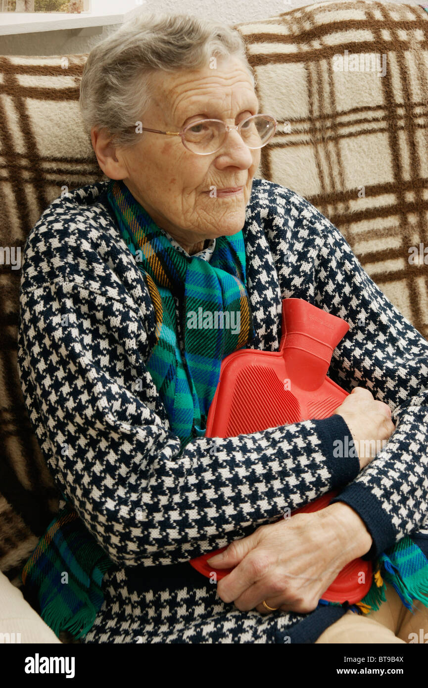 Donna anziana mantenendo calda in inverno indossando una spessa cardigan con bottiglie di acqua calda per salvare getting ipotermia Foto Stock
