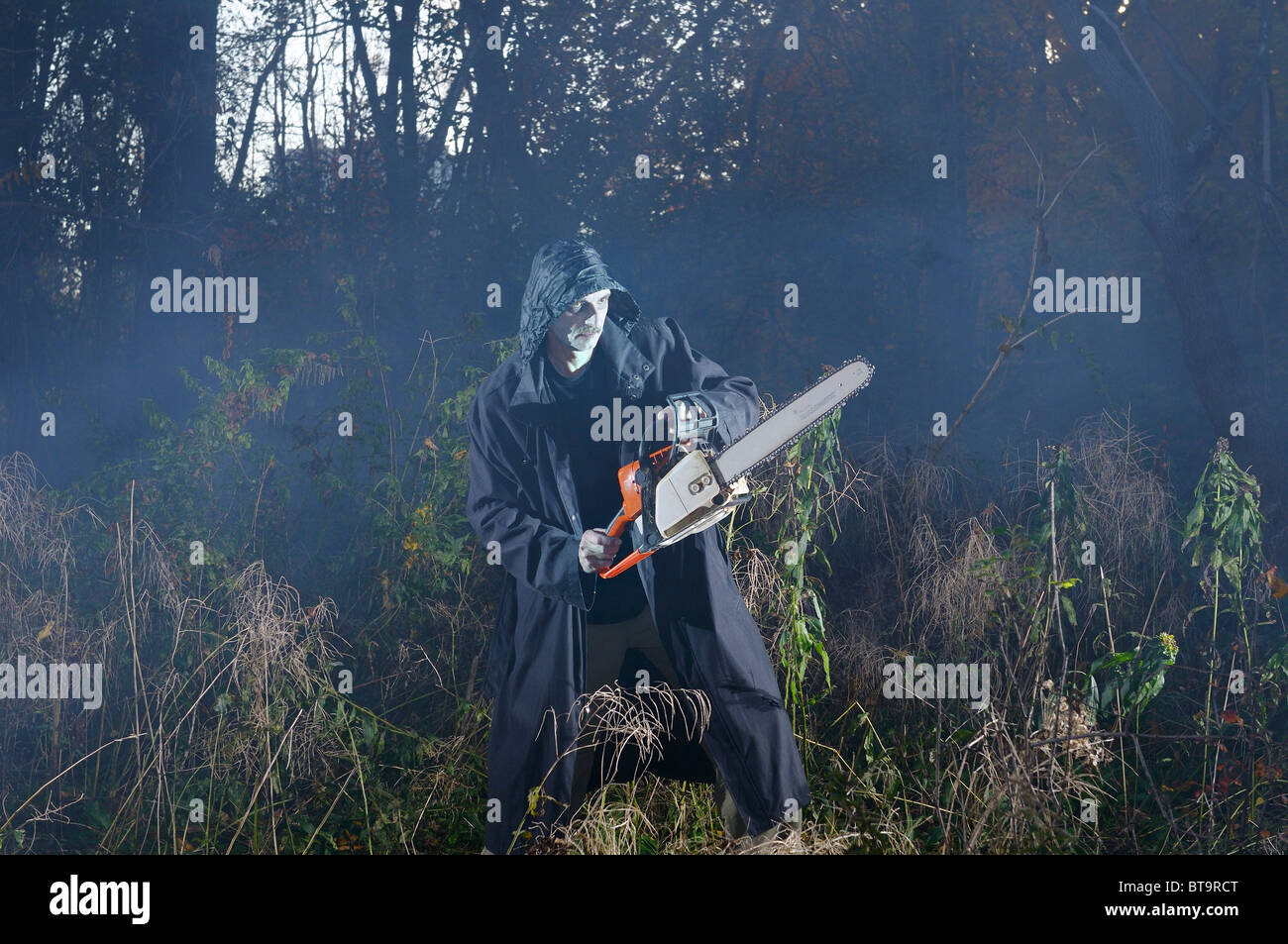 Scary Sinister man in black coat con una sega a nastro in un bosco nebbioso nella caduta di Halloween in un burrone di Toronto Foto Stock