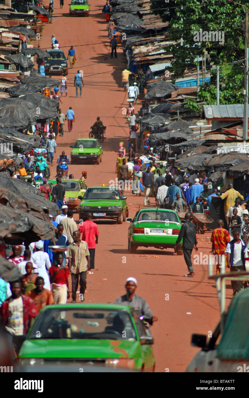 Rosso su strada sterrata e verde taxi nella città dell'uomo, Costa d Avorio, Africa occidentale Foto Stock