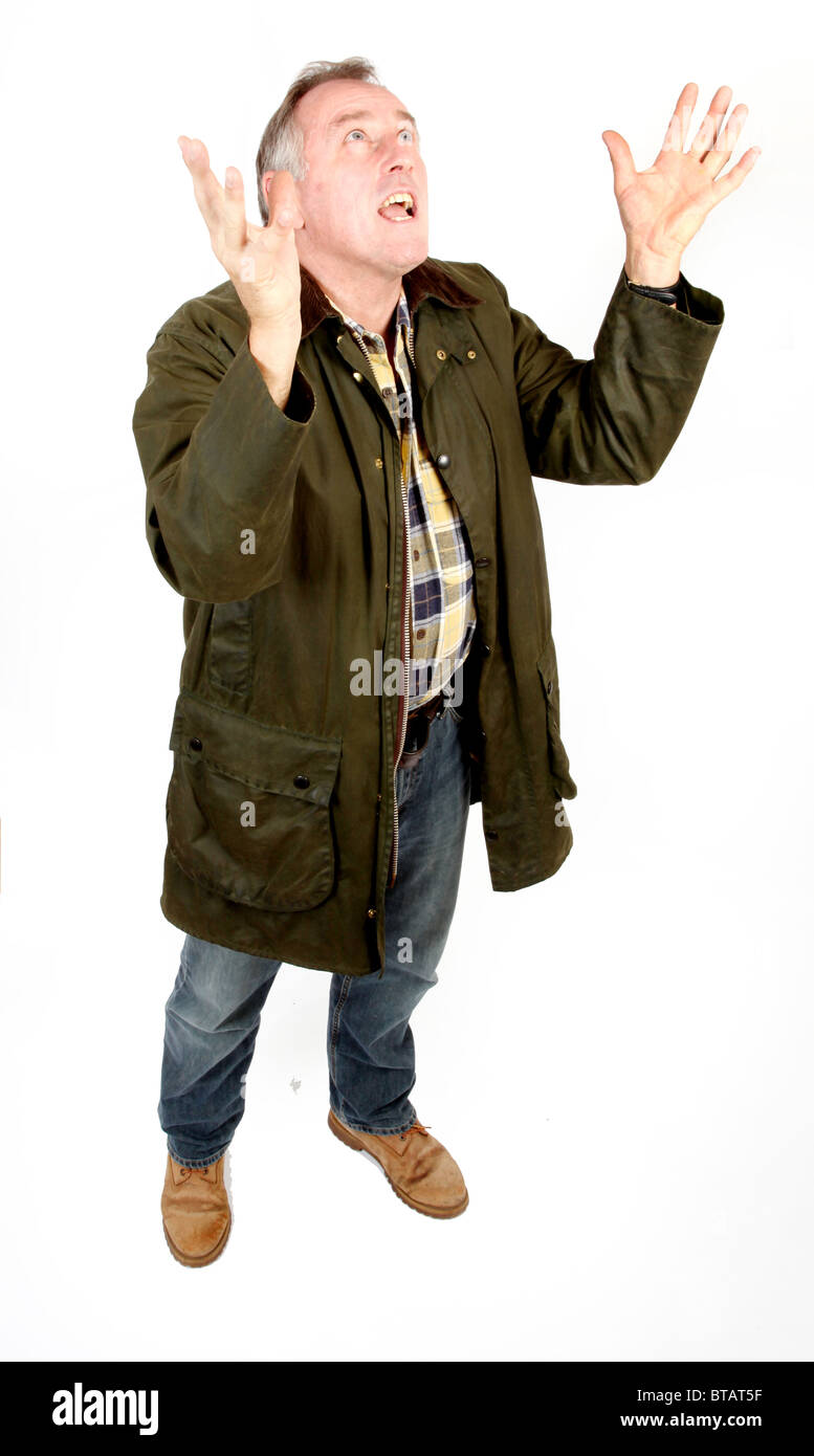 Uomo in 50s che indossa una giacca verde, jeans e stivali ha le braccia sollevate in merito a prendere qualcosa Foto Stock