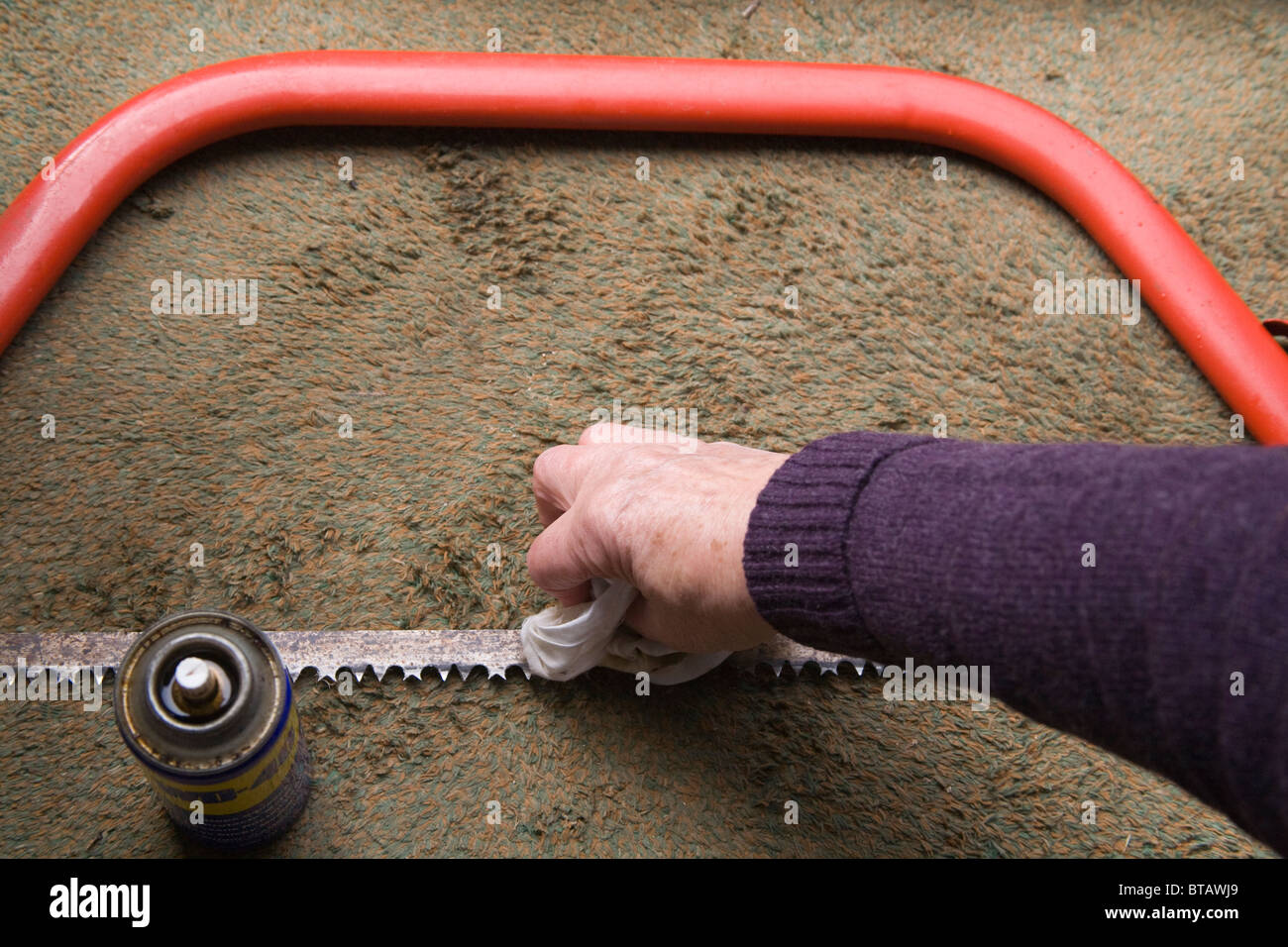 Chiudere fino a mano panno holding tergi WD 40 sul red lama per sega ad arco per pulire la ruggine Foto Stock