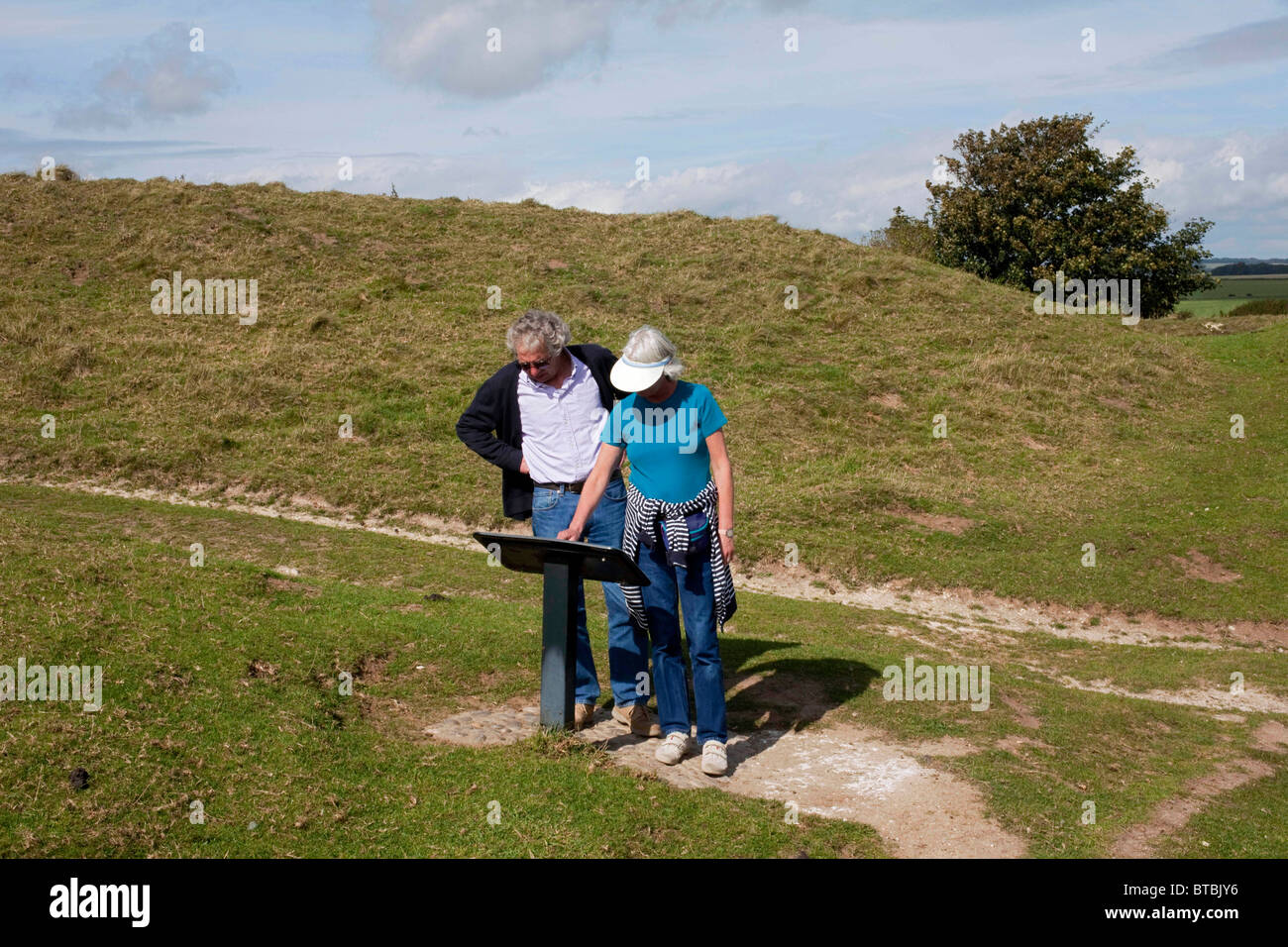 Una coppia in pensione alla ricerca di una scheda di informazioni all'età del ferro hill fort di Maiden Castle, Dorchester, Dorset. DAVID MANSELL Foto Stock