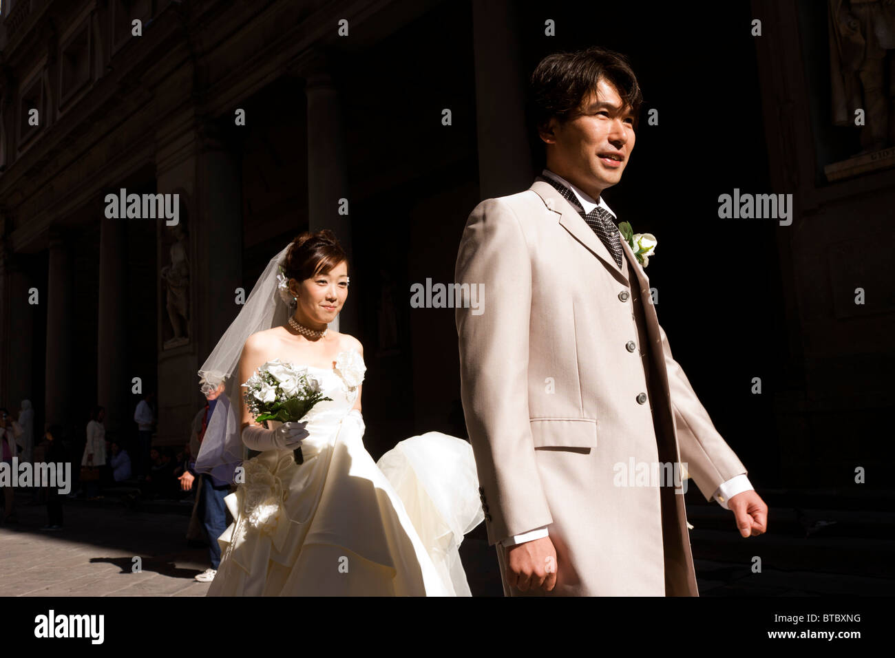 Sposa cinese cammina dietro il suo nuovo marito durante il servizio fotografico a piedi a Firenze Piazza degli Uffizi. Foto Stock