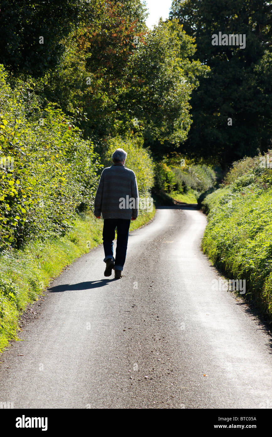 Uomo a camminare lungo una strada di campagna su una soleggiata giornata autunnale Foto Stock