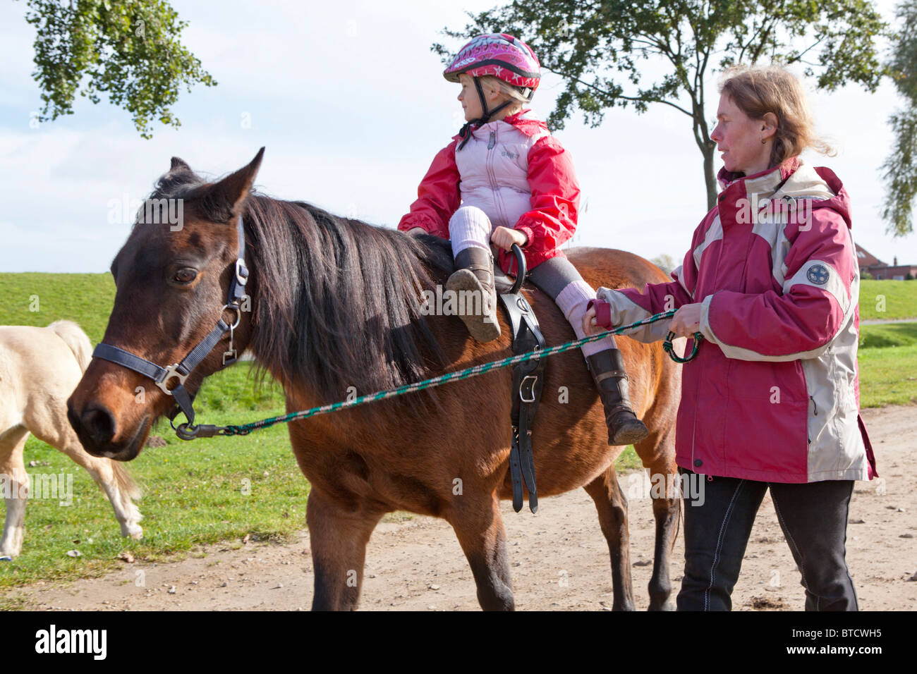 Piccola ragazza a cavallo di un pony in sella laterale Foto Stock