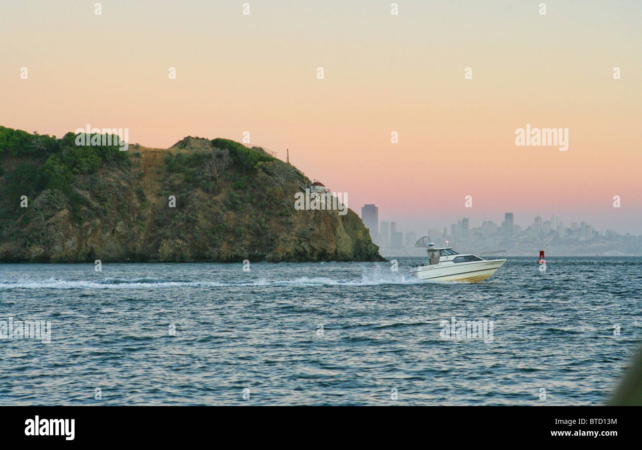 Un motoscafo con attrezzatura da pesca attraversando la baia di San Francisco al tramonto con Angel Island e lo skyline della città in background Foto Stock