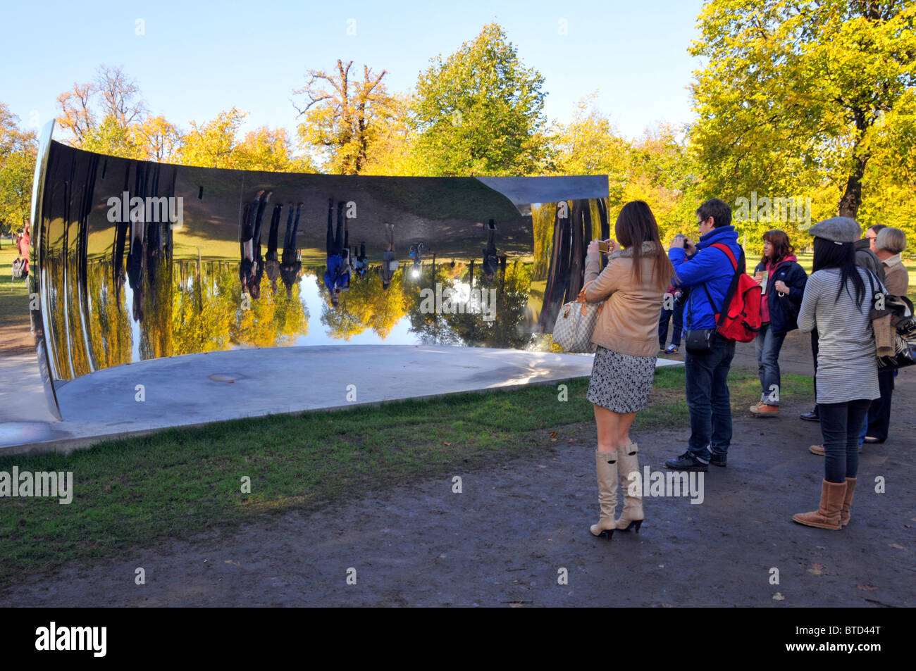 I turisti che visitano i Kensington Gardens hanno visto immagini riflesse di se stessi in uno degli specchi Anish Kapoor Sky Mirrors C Curve London Inghilterra UK Foto Stock