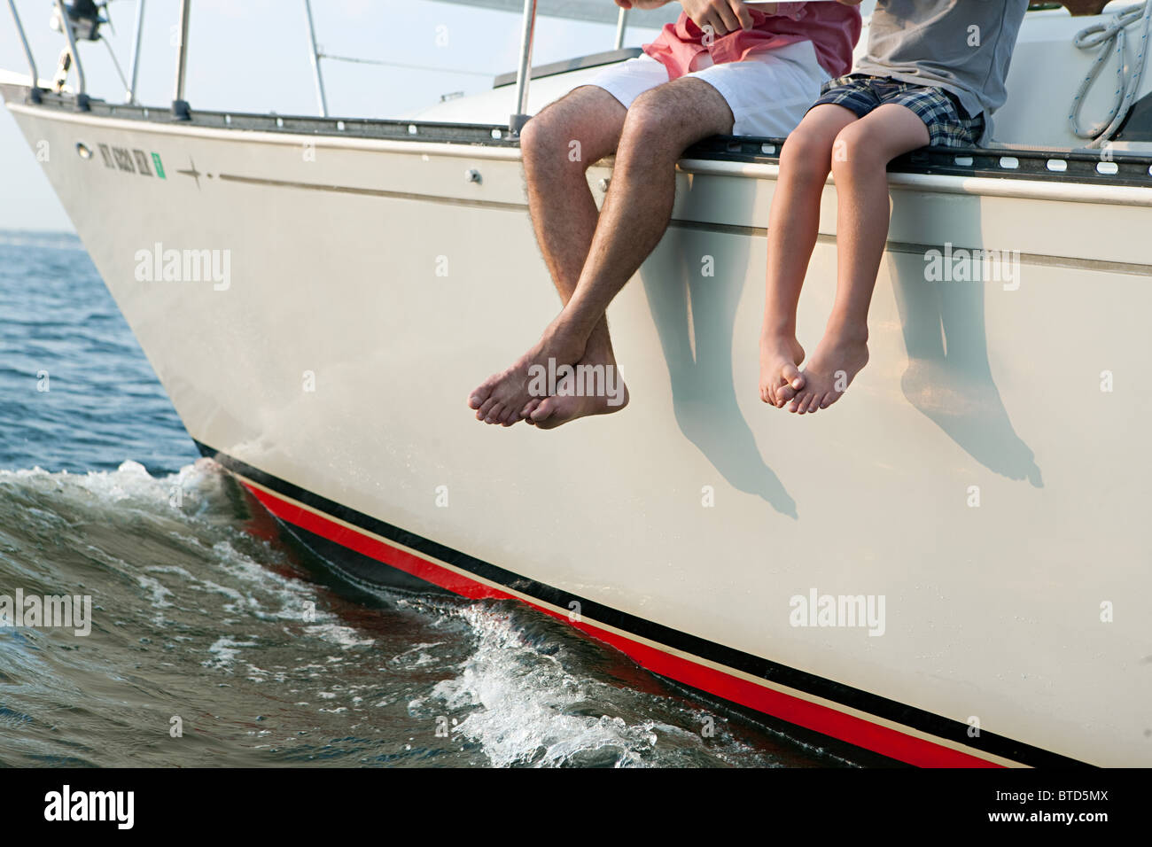 Padre e figlio seduti su yacht, gambe penzolanti Foto Stock