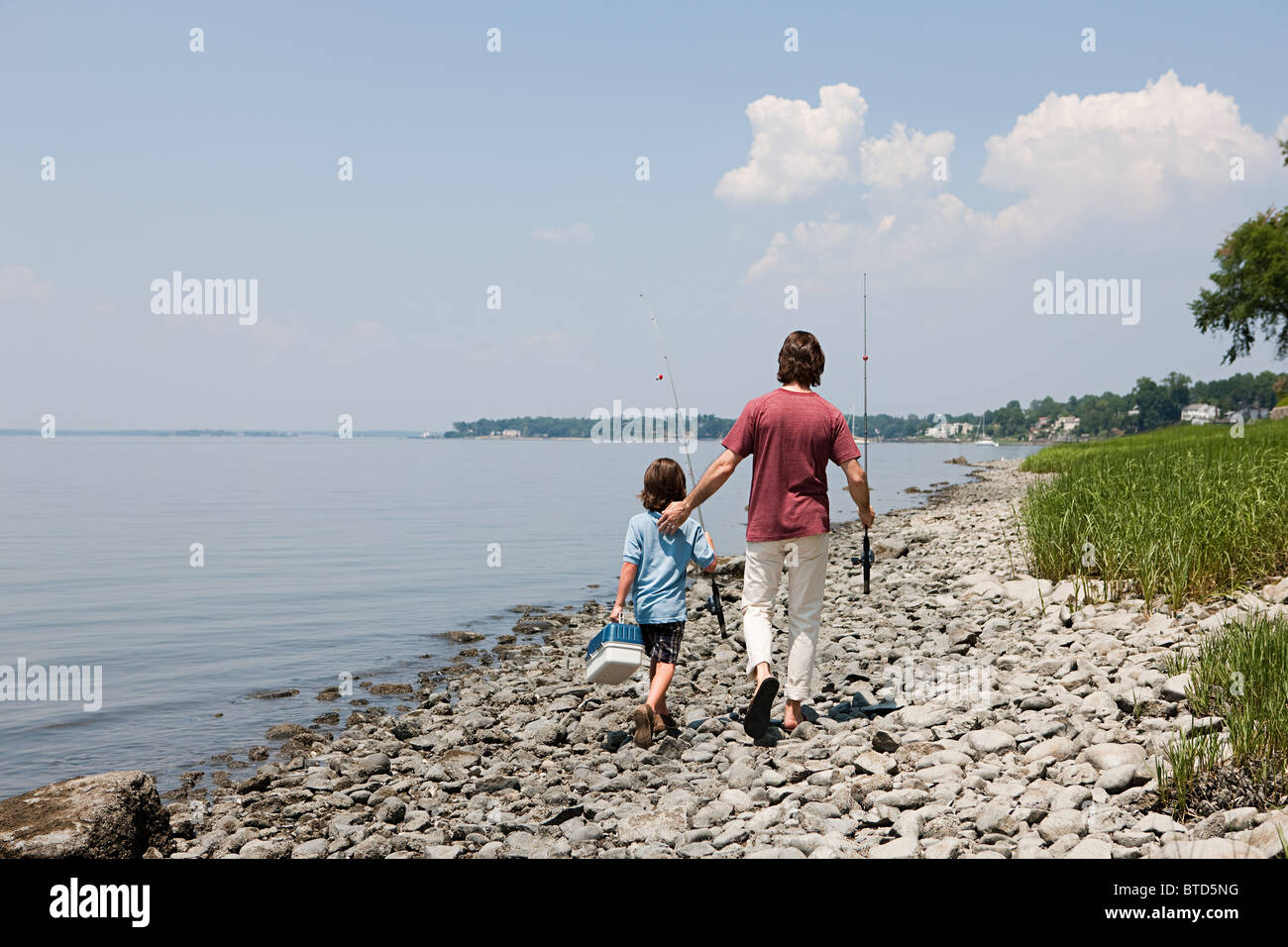 Padre e figlio a piedi lungo la spiaggia con canne da pesca Foto Stock