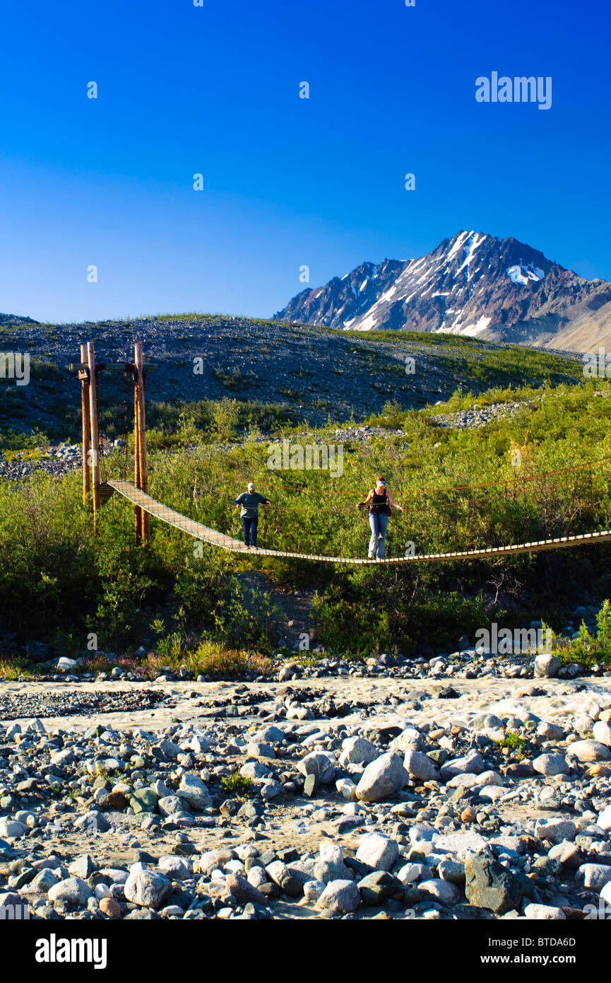 Gli escursionisti attraversare un ponte di sospensione su College Creek sul loro modo al ghiacciaio Gulkana, centromeridionale Alaska Foto Stock