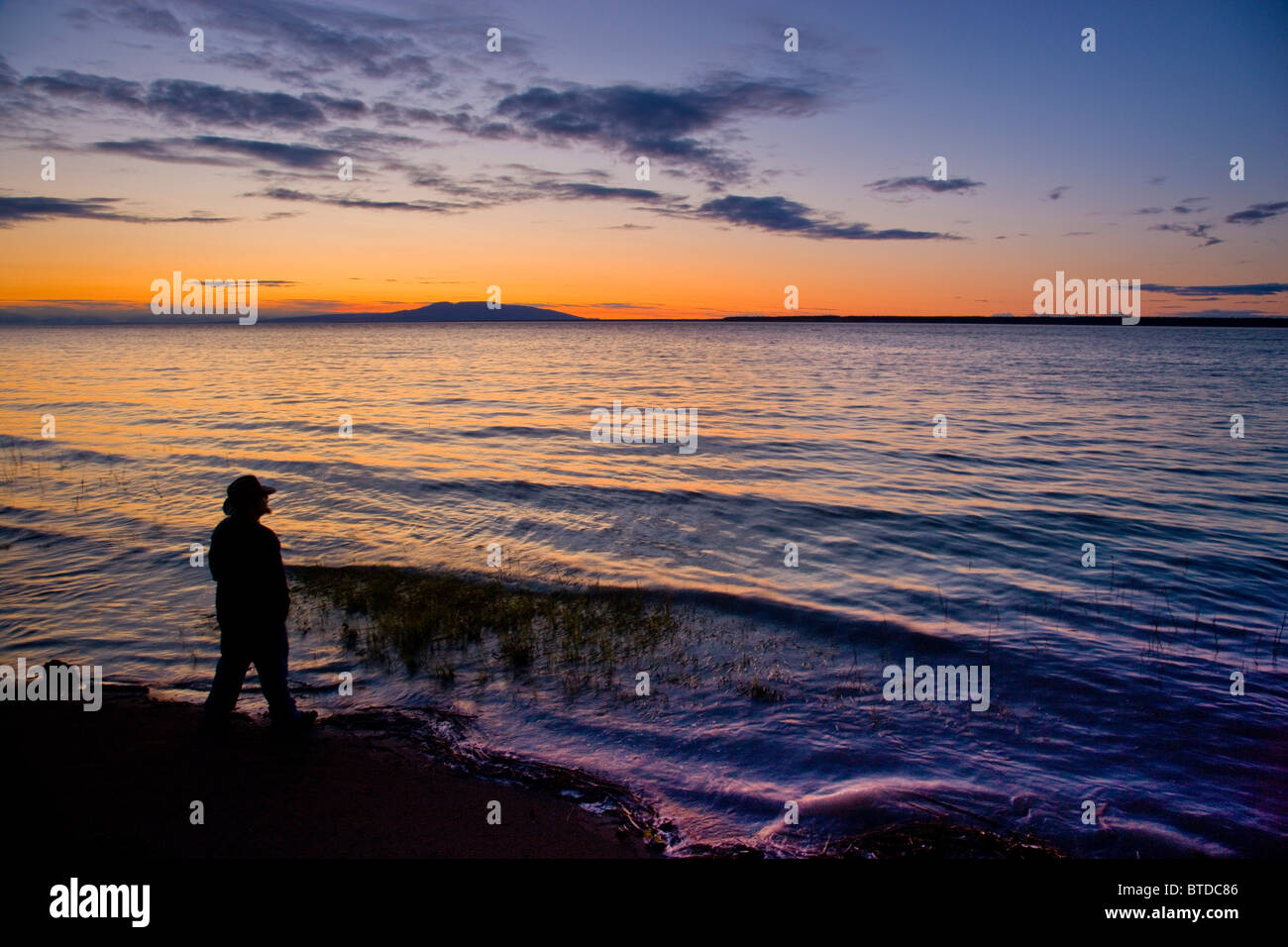 Silhouette di un uomo in piedi sulla riva del Knik Arm mentre guardate il tramonto sul Monte Susitna, Alaska, estate Foto Stock