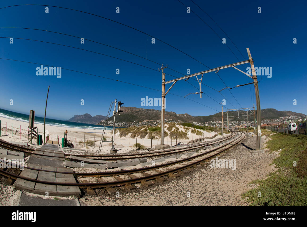 Fish-eye di binari ferroviari in esecuzione passato Fish Hoek Beach e una vista della Table Mountain in background Foto Stock