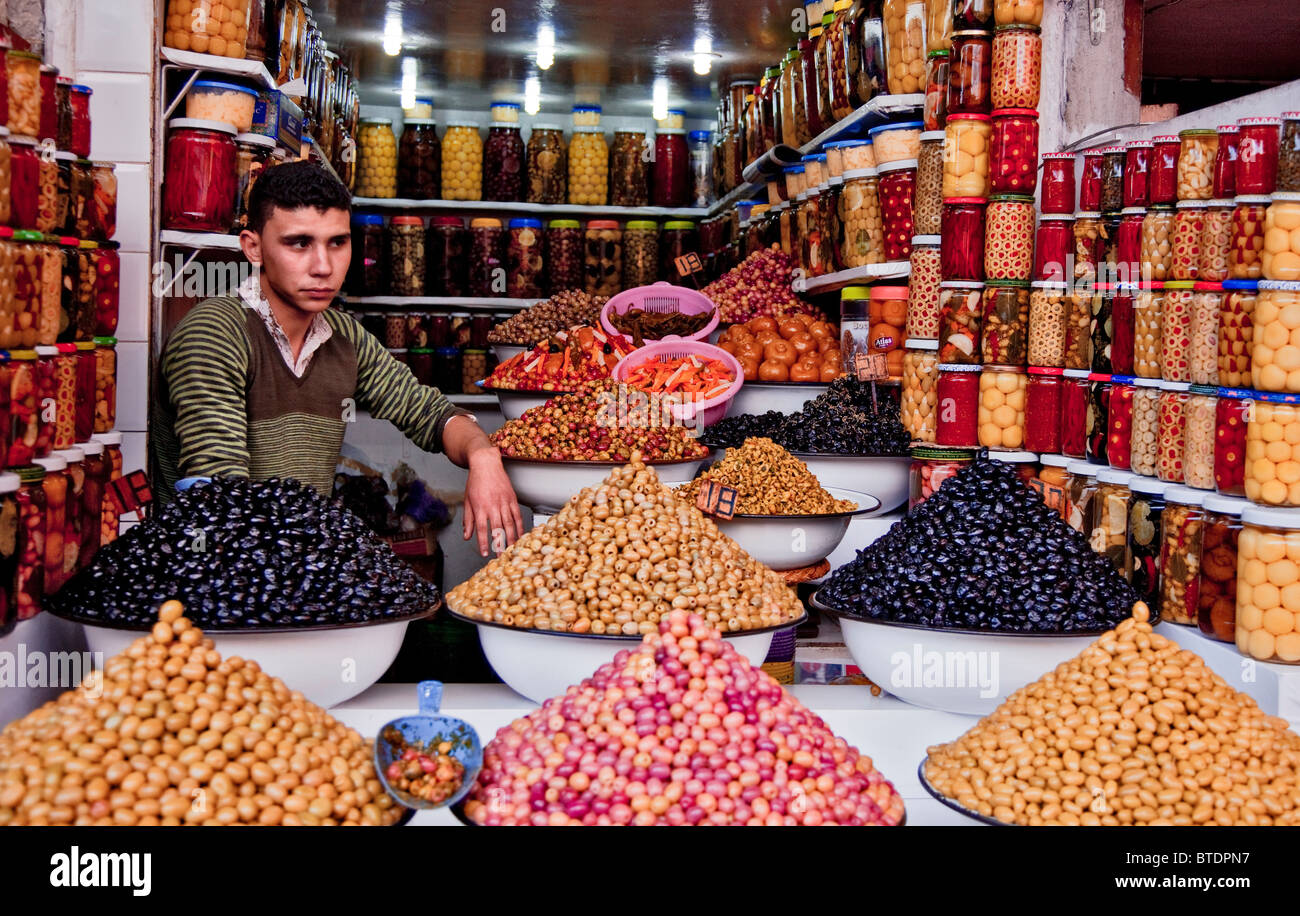 Giovani magazziniere presso il mercato di Marrakech circondato da bottiglie di conserve di frutta e di cumuli di frutti e bacche di bocce Foto Stock