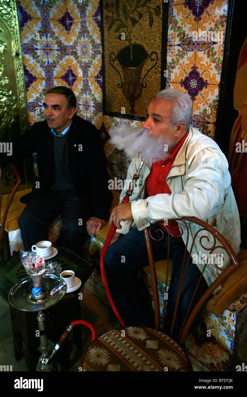 Uomo di fumare narghilè tradizionali tubi di acqua in corrispondenza di una caffetteria nella medina di Tunisi. Foto Stock