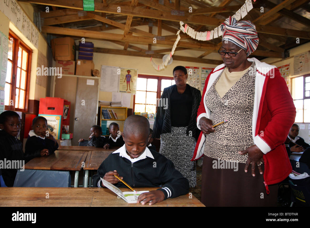 I giovani della scuola ragazzo lettura mentre il suo insegnante si affaccia su di un territorio rurale Kwazulu Natal a scuola Foto Stock