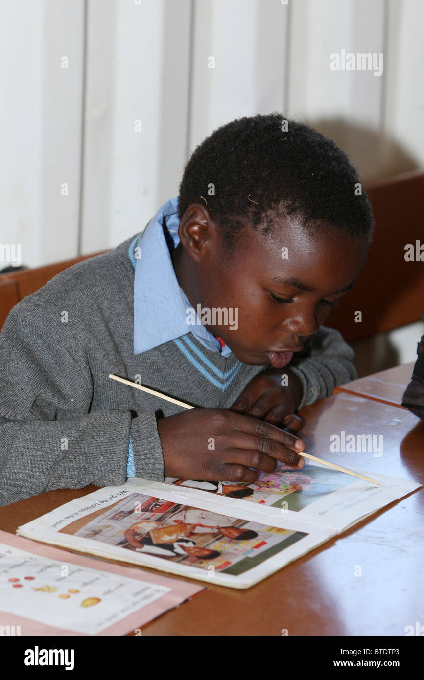 Giovane pupillo utilizzando un puntatore per imparare a leggere in una zona rurale Kwazulu Natal a scuola Foto Stock