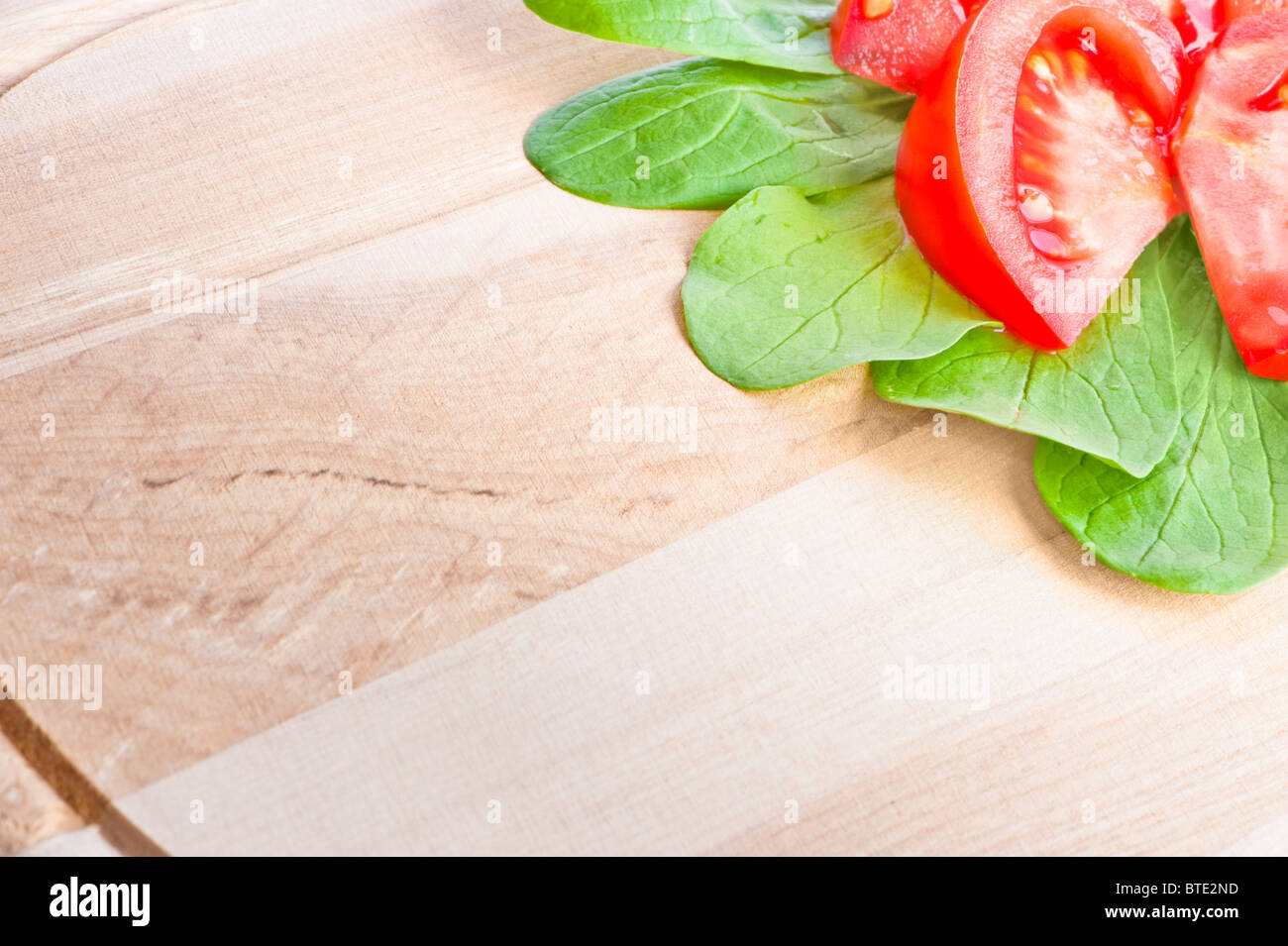 Tagliere in legno close-up con fette di pomodori rossi e verdi di lattuga agnelli nell'angolo. Copyspace sul bordo di taglio. Foto Stock