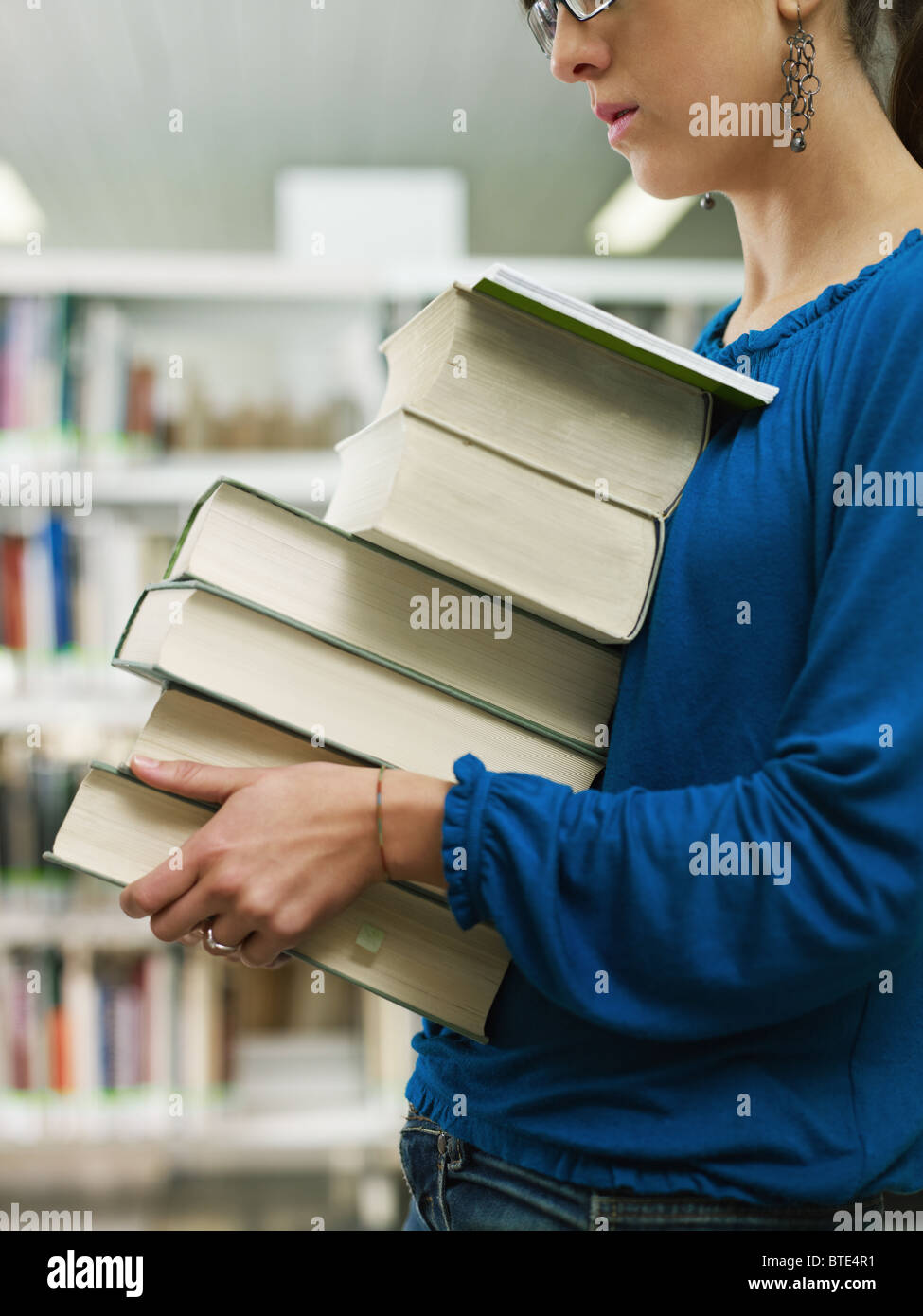 Donna che mantiene pila di libri in biblioteca Foto Stock