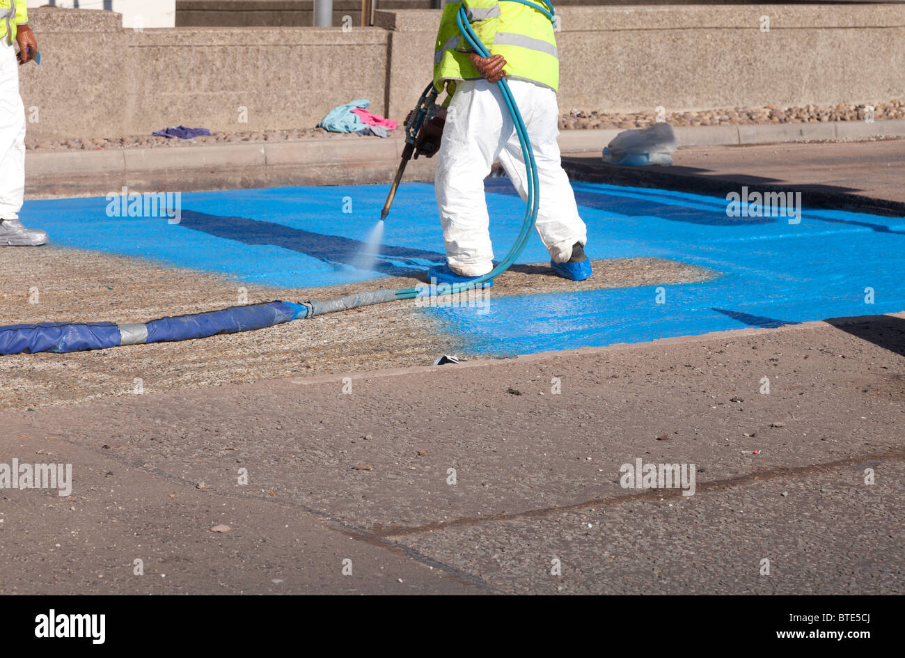 Immagine di un team di dipendenti una spruzzatura di 2mm di PVC strato di membrana di un proprietario Impermeabilizzante spray durante la strada re-riporto. Foto Stock