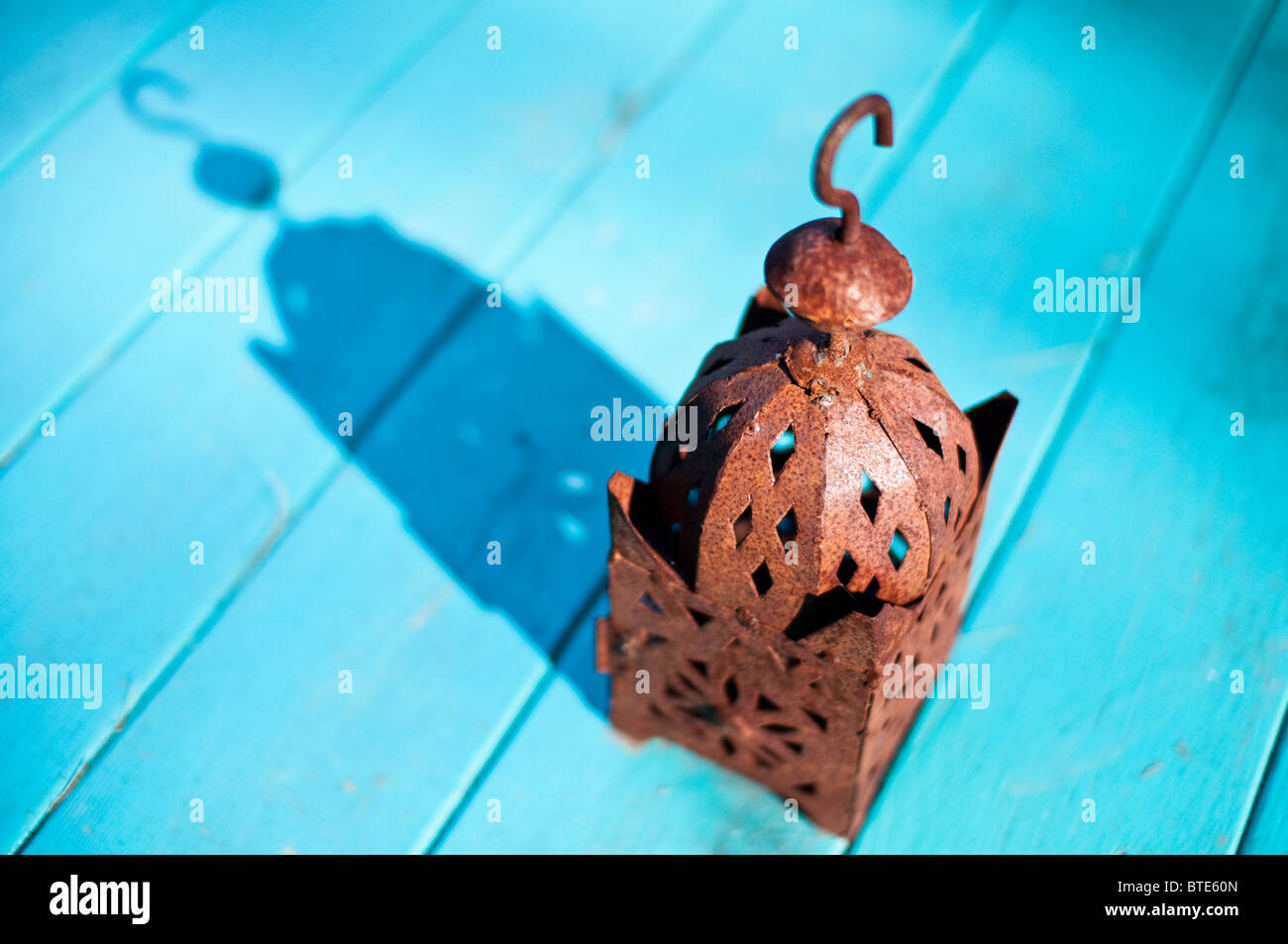 Un arrugginito Lanterna da esterno si siede al sole su un blu Tavolo da giardino. Foto Stock