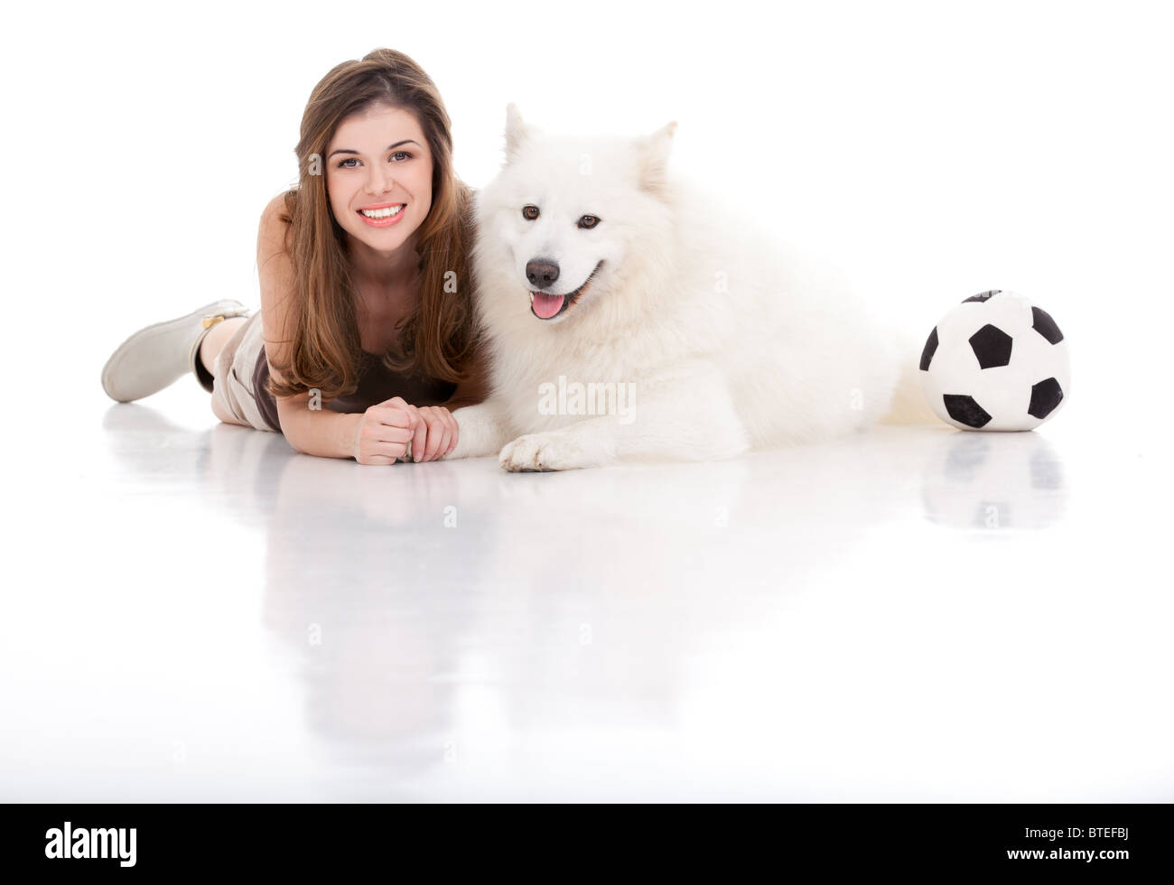 Un studio immagine di una giovane donna con un cane bianco, sia in posa da seduto il loro ventre, tenendo le mani, sorridendo con un calcio sul Foto Stock