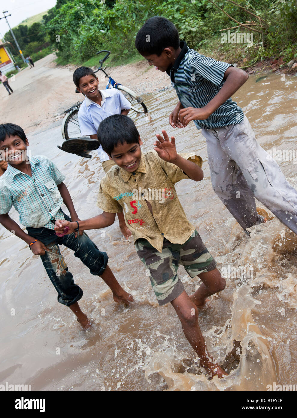 Bambini indiani jumping e spruzzi di acqua su una strada allagata in Andhra Pradesh, India Foto Stock