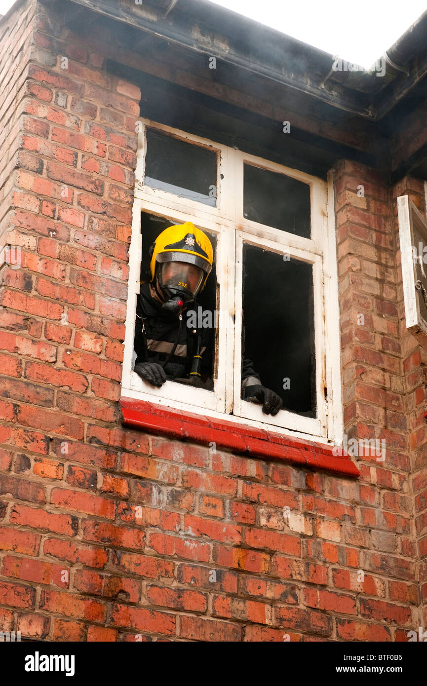 Fireman in BA guarda fuori della finestra della camera in casa di fuoco. Fire & Rescue Service UK Foto Stock