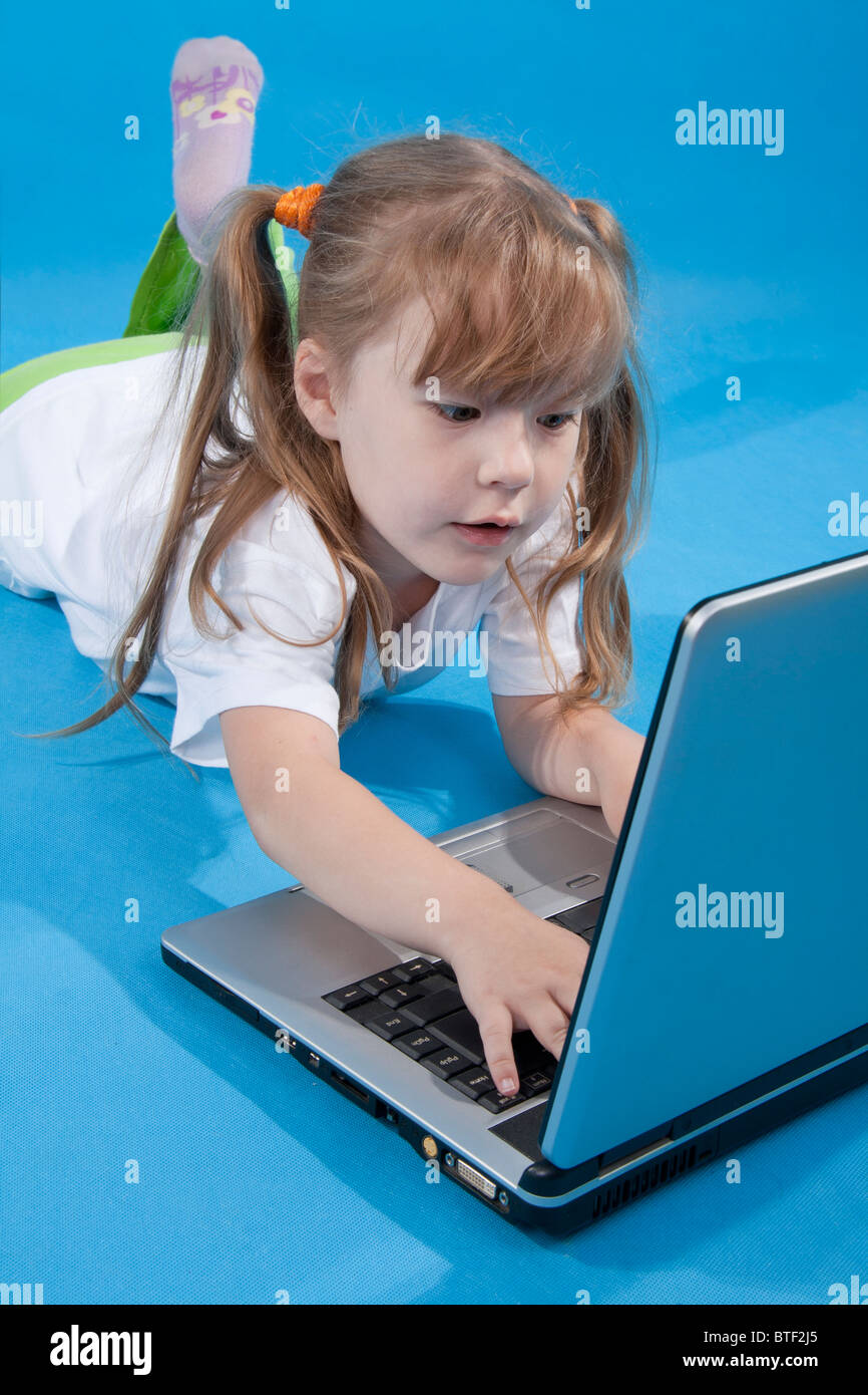 La bambina è di usare il computer su sfondo blu Foto Stock