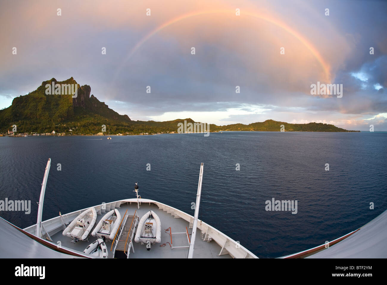 Visto da una nave, un tardo pomeriggio rainbow passa sopra l'isola vulcanica di Bora Bora. Polinesia francese, Oceano Pacifico. Foto Stock